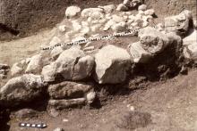 In primo piano, massi di pietra facenti parte del muro di un'abitazione retica della media età del ferro, sullo sfondo pietre più piccole che lastricavano l'ingresso dell'edificio, riportate alla luce nel 1977 sotto la fattoria del Col de Flam. 