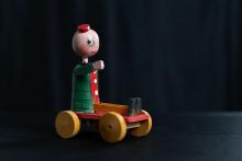 Comic character Fortunello as a turned and painted toy sitting on a board on wheels that moves his legs up and down when pushed